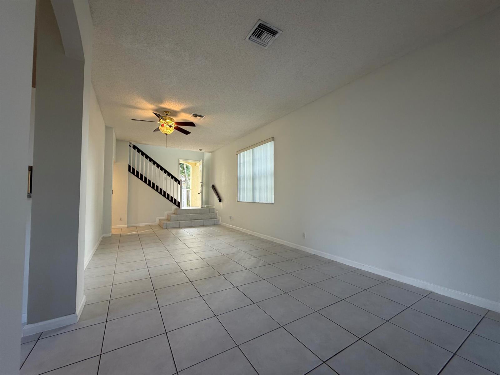 An empty living room with light tile flooring, white walls, and a staircase — 1848 Capeside, Wellington FL 33414, WELLINGTON, FL