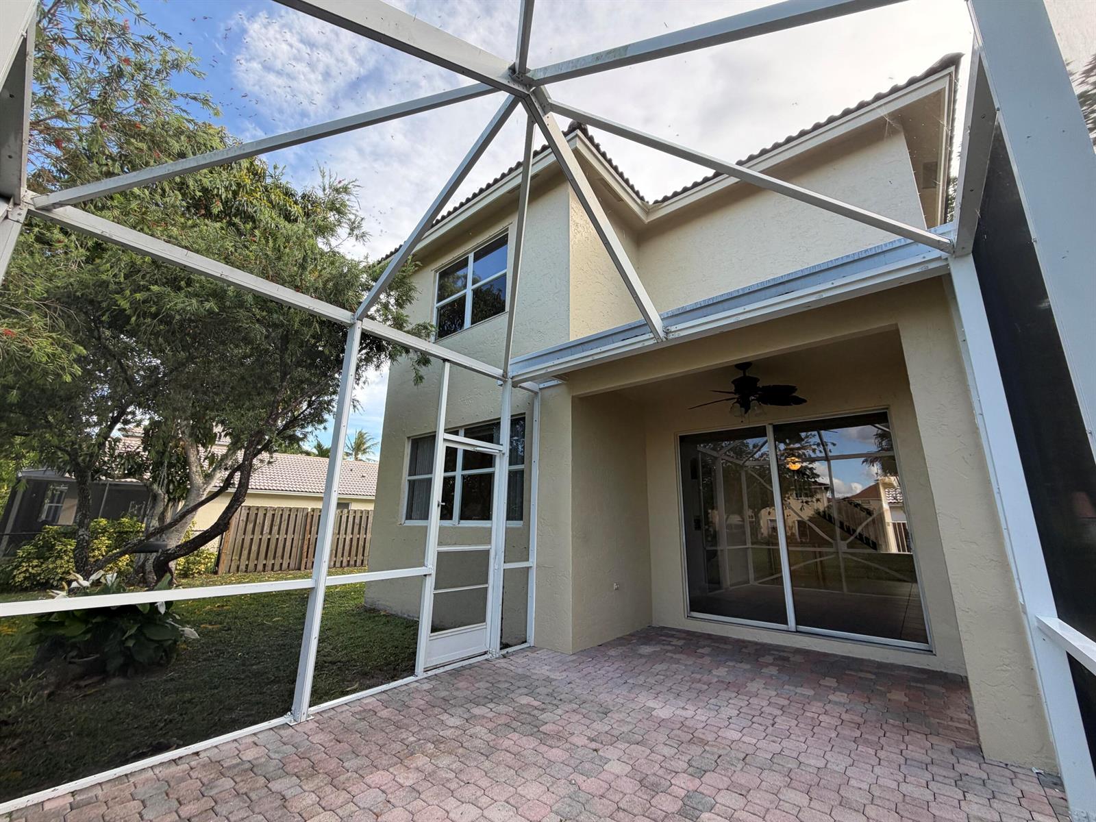A paved patio is enclosed by a screened-in lanai attached to a two-story stucco house — 1848 Capeside, Wellington FL 33414, WELLINGTON, FL