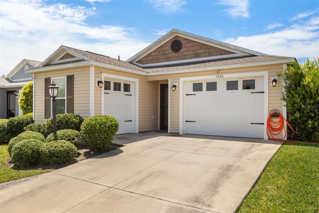 A single-story house with light yellow siding, a two-car garage, and a concrete driveway — 1930 RHETT ROAD, THE VILLAGES, FL