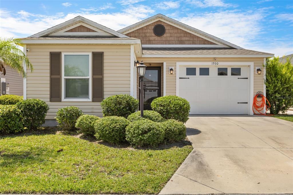 A single-story house with tan siding, a white garage door, and manicured landscaping — 1930 RHETT ROAD, THE VILLAGES, FL