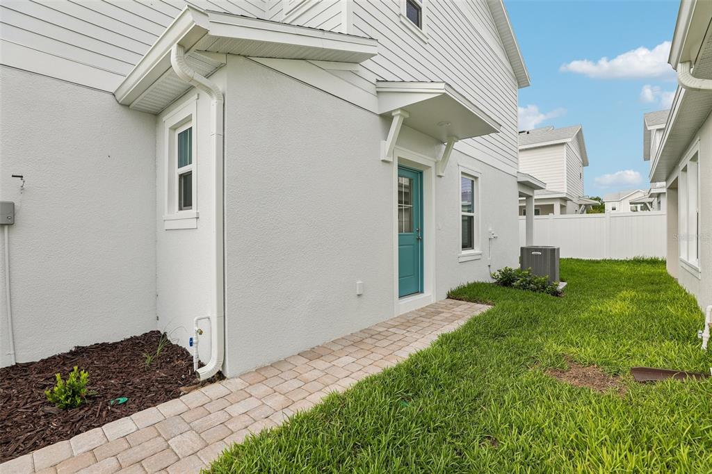 The exterior side of a house features a teal door, a paver walkway, and grass — 2704 MEADOW CREST DRIVE, ST CLOUD, FL