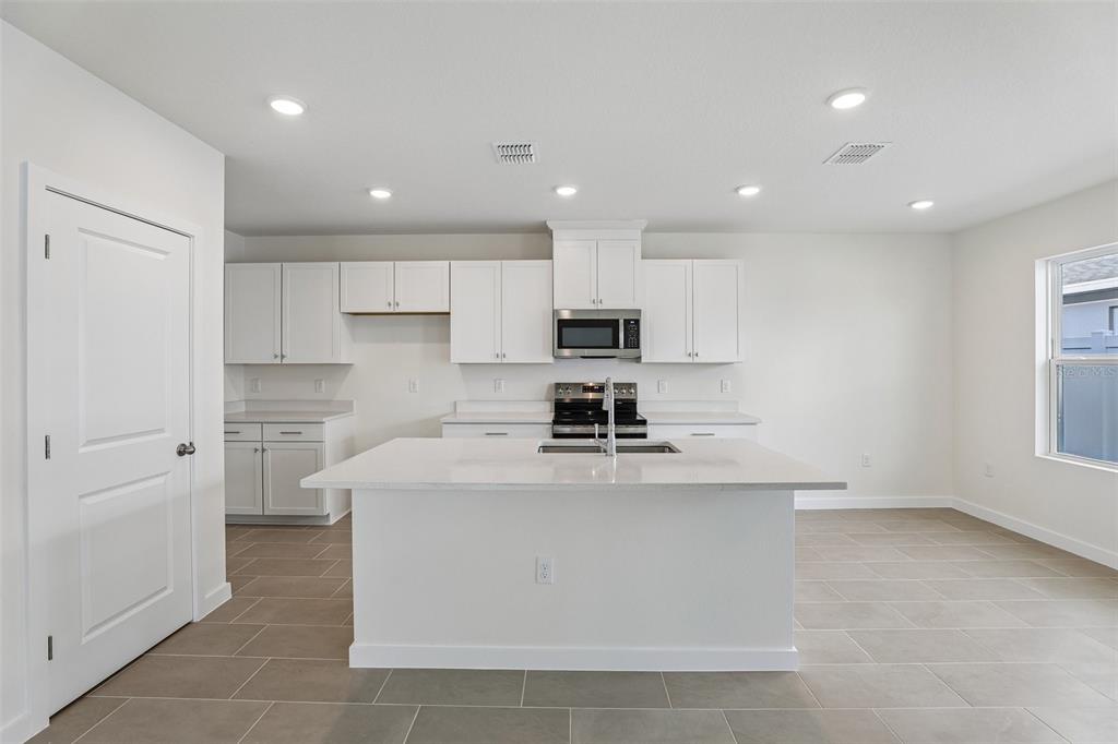 A modern kitchen features white cabinetry, a central island with a sink, and tile flooring — 2704 MEADOW CREST DRIVE, ST CLOUD, FL