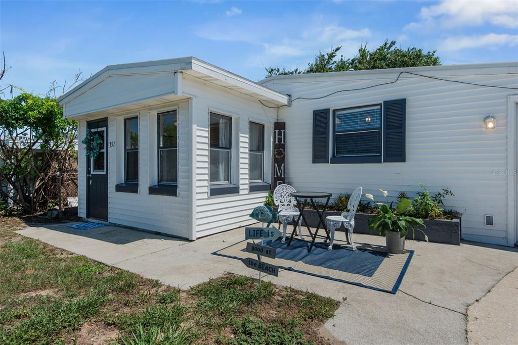 A white mobile home exterior features a small patio with a bistro set and sign — 151 HOLLAND ROAD, ORMOND BEACH, FL