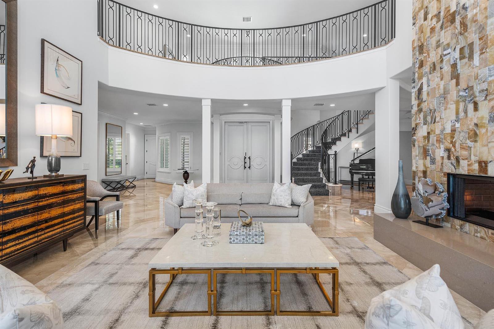 A spacious living room features a stone fireplace, a curved staircase, and a mezzanine balcony — 121 Royal Palm Way, Boca Raton FL 33432, BOCA RATON, FL