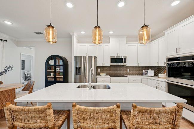 A modern kitchen features a large white quartz island, pendant lighting, and white cabinetry — 12036 LIMPKIN ROAD, WEEKI WACHEE, FL