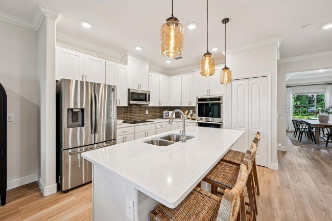 A modern kitchen features white cabinetry, a quartz-topped island, stainless steel appliances, and pendant lighting — 12036 LIMPKIN ROAD, WEEKI WACHEE, FL