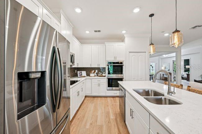 A modern kitchen features white cabinets, stainless steel appliances, a quartz island, and wood flooring — 12036 LIMPKIN ROAD, WEEKI WACHEE, FL