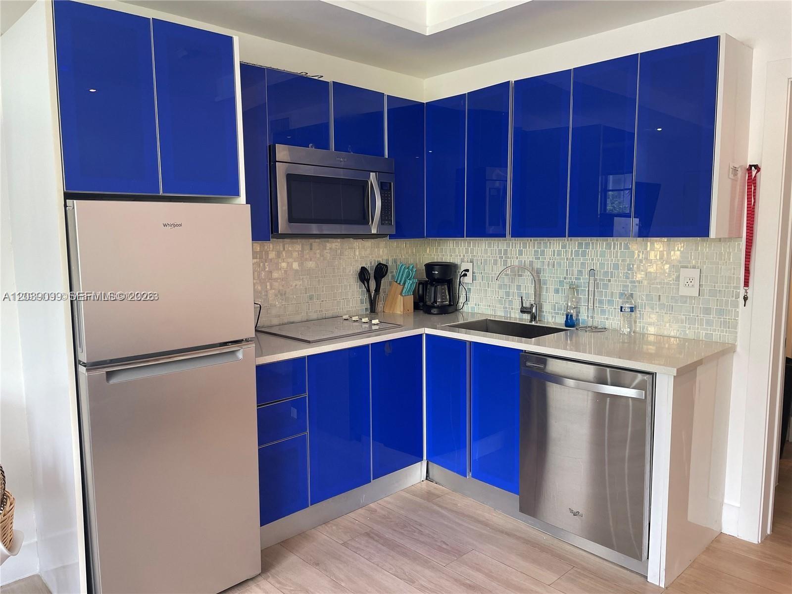 A kitchen features glossy blue cabinets, stainless steel appliances, and a light-colored tile backsplash — 700 16th St # 108, Miami Beach FL 33139, MIAMI BEACH, FL