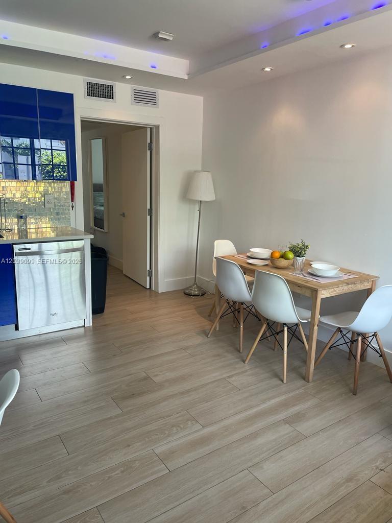 A kitchen and dining area feature light wood flooring, white chairs, and blue cabinets — 700 16th St # 108, Miami Beach FL 33139, MIAMI BEACH, FL