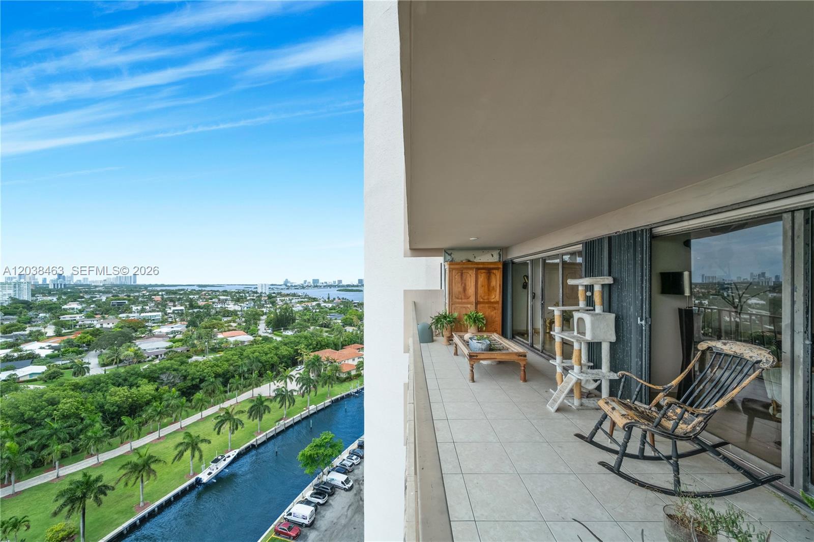 A high-rise balcony features a rocking chair, cat tree, and views of a canal — 1800 NE 114th St # 1811, Miami FL 33181, MIAMI, FL