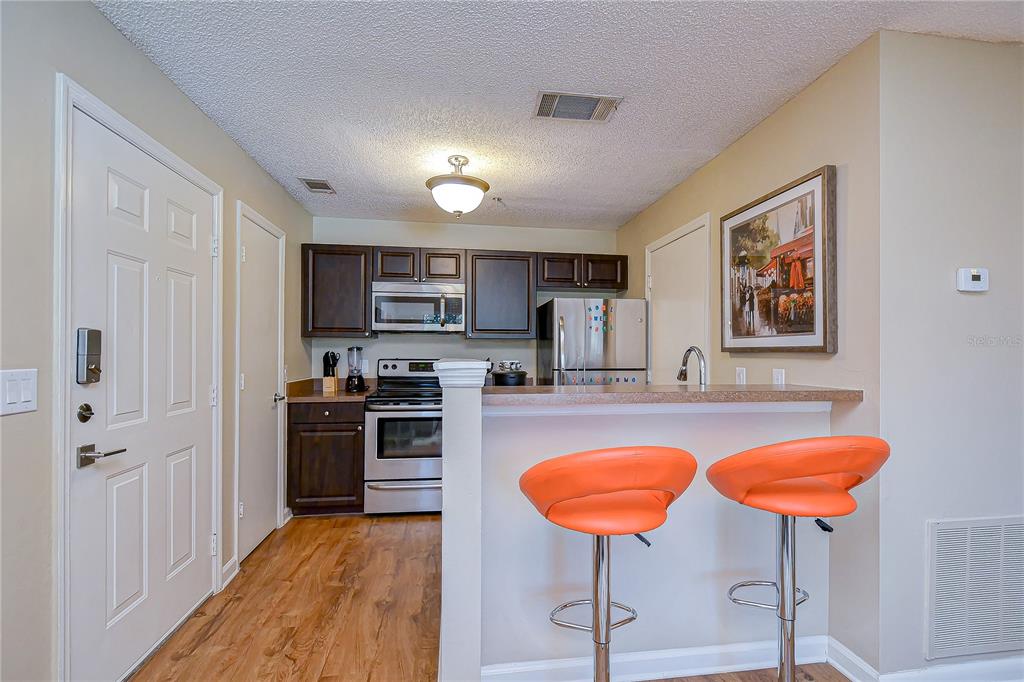 A kitchen features dark wood cabinets, stainless steel appliances, and two orange bar stools — 11901 4TH STREET N UNIT 4206, ST PETERSBURG, FL