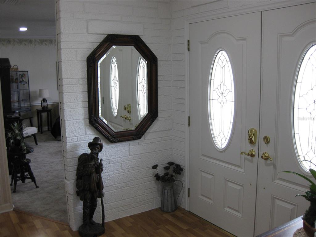 An entryway features a white brick wall, an octagonal mirror, and a wooden statue — 7026 LENAPE CIRCLE, NEW PORT RICHEY, FL