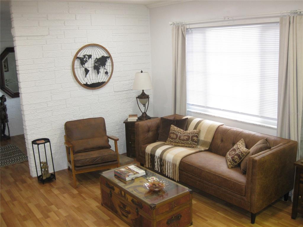 A living room features a white brick wall, brown leather sofa, armchair, and wooden flooring — 7026 LENAPE CIRCLE, NEW PORT RICHEY, FL