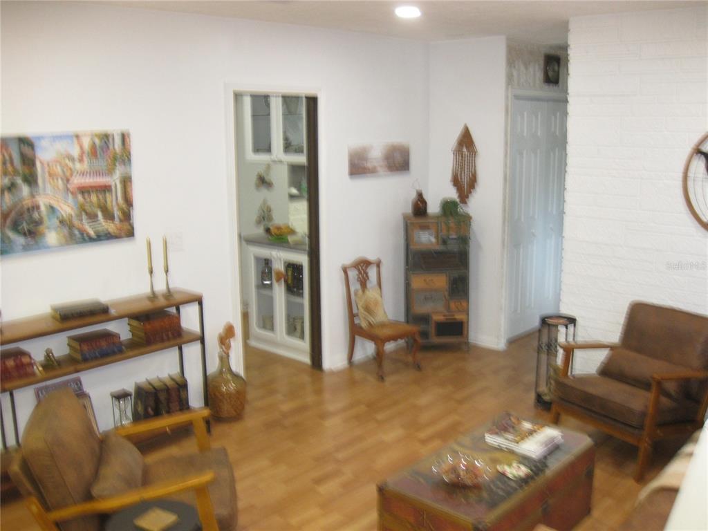 A living room features wood-look flooring, a brick wall, two armchairs, and a wooden chest — 7026 LENAPE CIRCLE, NEW PORT RICHEY, FL