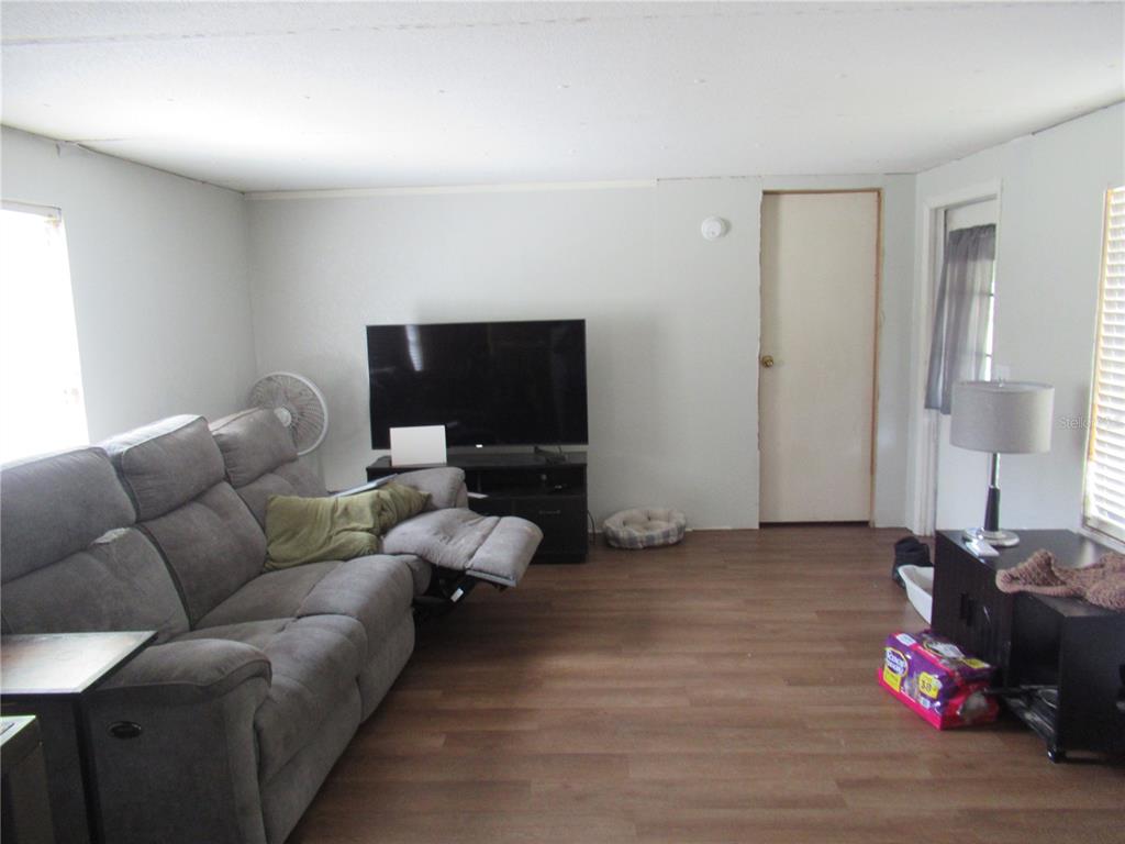 A living room features gray wood-look flooring, a gray reclining sofa, and a television stand — 7814 TURKEY CREEK ROAD, PLANT CITY, FL
