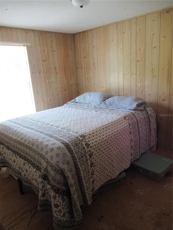 A bedroom features wood-paneled walls, a patterned bedspread, and an unfinished subfloor — 7814 TURKEY CREEK ROAD, PLANT CITY, FL