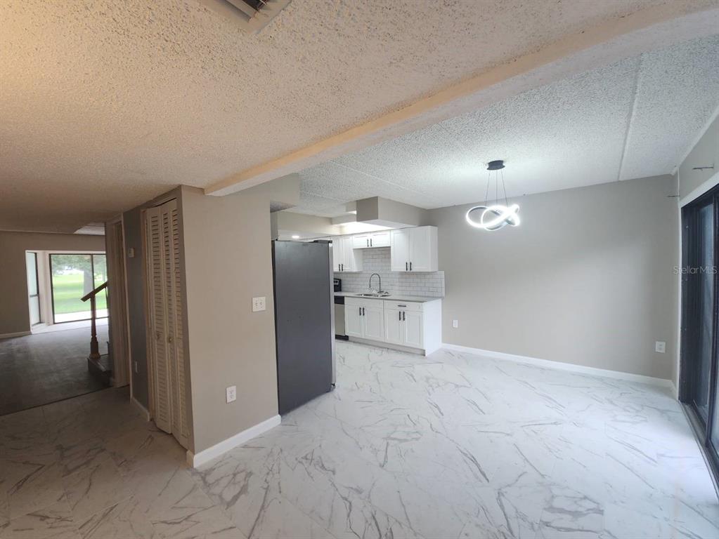 A kitchen with white cabinets and a black refrigerator opens to a tiled dining area — 5312 CYPRESS CREEK DRIVE UNIT 104, ORLANDO, FL