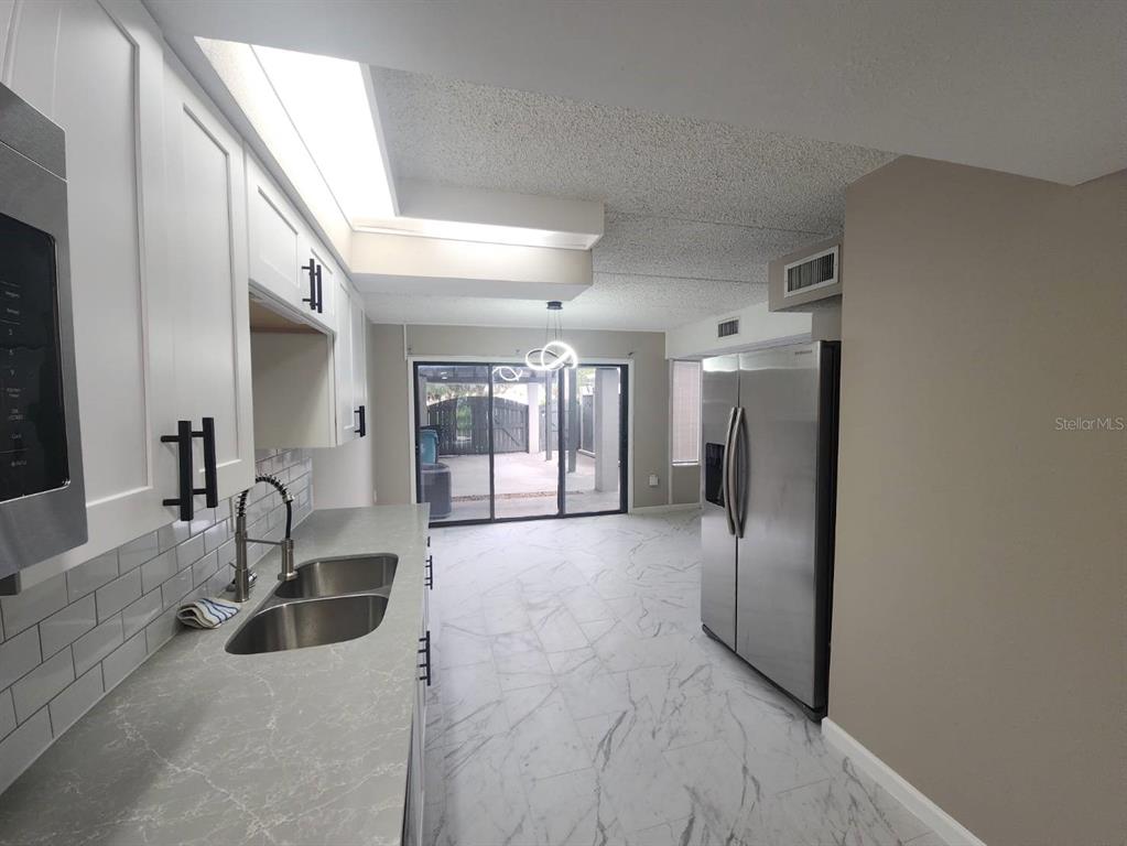 A kitchen with white cabinets, gray countertops, stainless steel appliances, and marble-look tile flooring — 5312 CYPRESS CREEK DRIVE UNIT 104, ORLANDO, FL