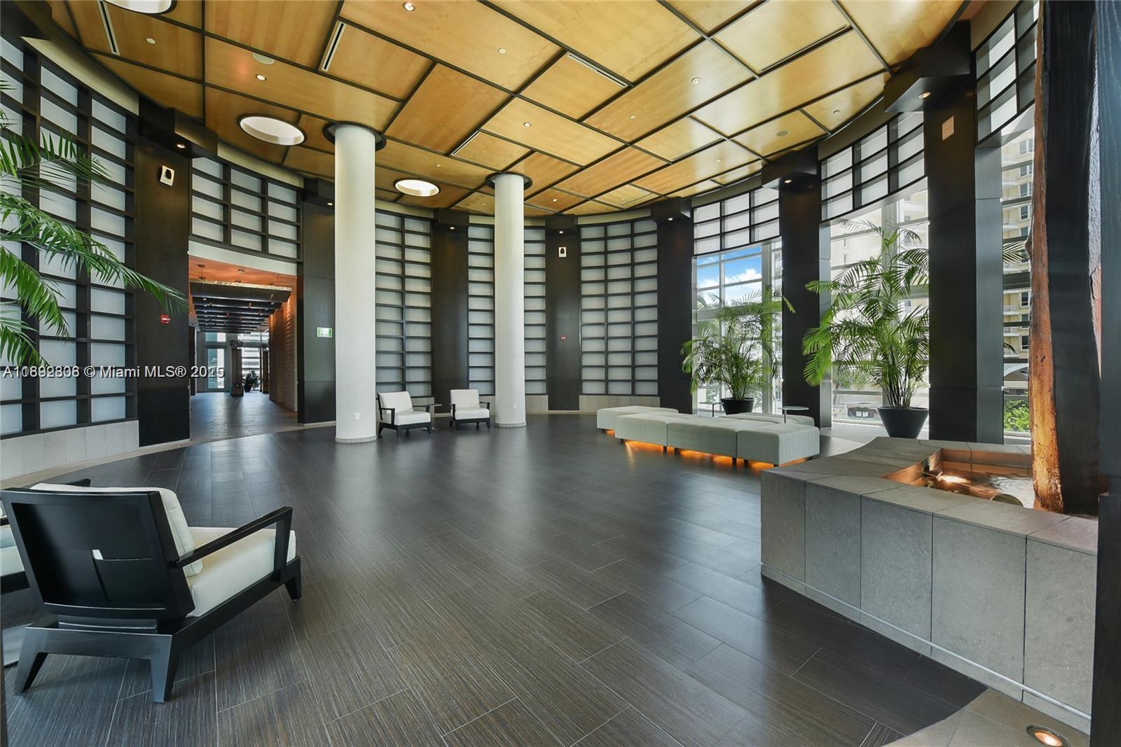 A spacious modern lobby features dark tile floors, white columns, and a wood-paneled ceiling — 900 Brickell Key Blvd # 2602, Miami FL 33131, MIAMI, FL