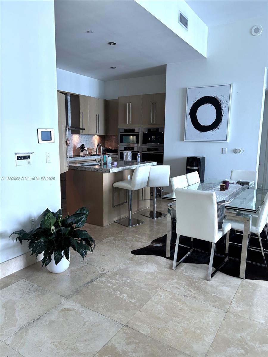 A modern kitchen with light wood cabinets and a dining area with white chairs — 900 Brickell Key Blvd # 2602, Miami FL 33131, MIAMI, FL