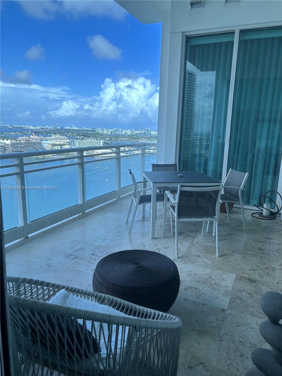 A balcony with outdoor furniture overlooks a bay and a city skyline — 900 Brickell Key Blvd # 2602, Miami FL 33131, MIAMI, FL