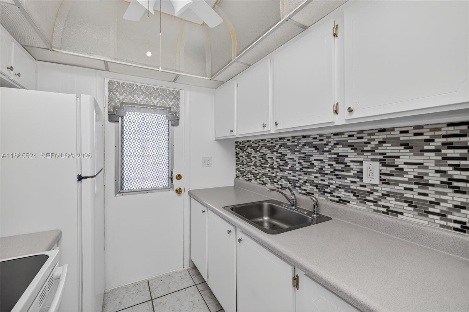A kitchen features white cabinets, a gray countertop, a mosaic backsplash, and a white door — 16901 NE 13th Ave # 210, Miami FL 33162, MIAMI, FL