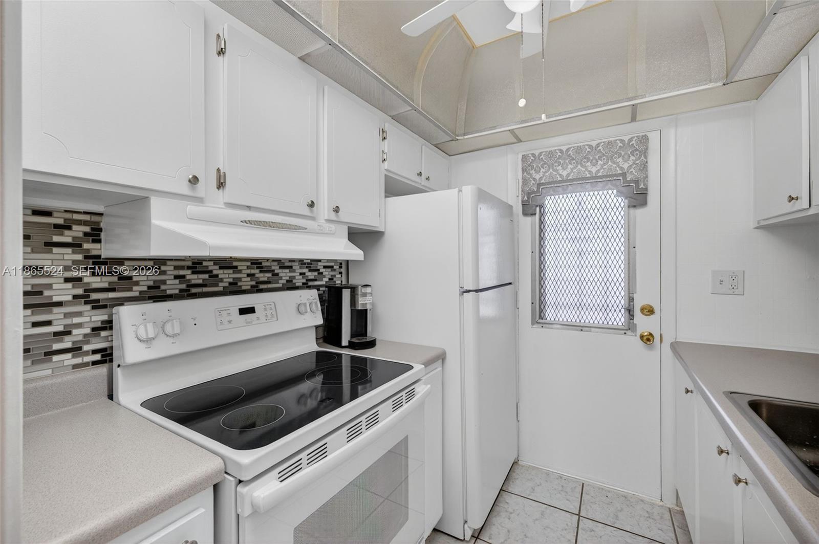 A white kitchen features a glass-top stove, white appliances, and a patterned tile backsplash — 16901 NE 13th Ave # 210, Miami FL 33162, MIAMI, FL