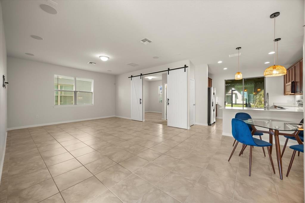 An open-concept living area features tile flooring, white walls, sliding barn doors, and a kitchen — 2716 VISTA VERDE LANE, KISSIMMEE, FL