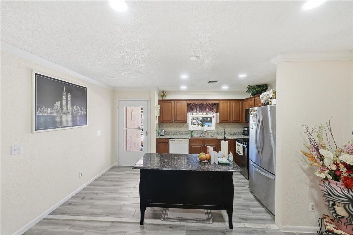 A kitchen features wood cabinets, a granite-topped island, stainless steel appliances, and wood-look flooring — 6531 SE Federal Highway SE # Q108, Stuart FL 34997, STUART, FL