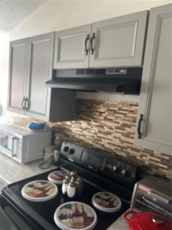 A kitchen features gray cabinets, a black range, and a multi-colored mosaic tile backsplash — 431 EAGLE DRIVE, POINCIANA, FL