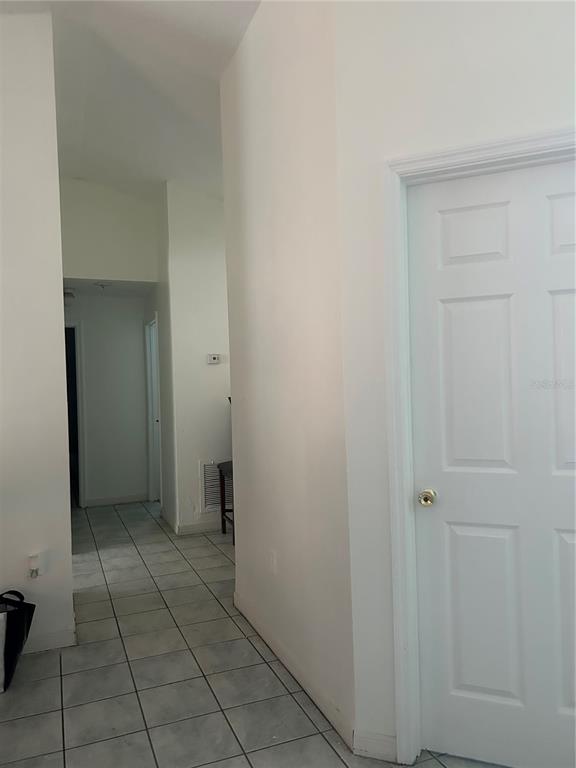 A hallway with light-colored tile flooring leads toward a doorway, with a white door on the right — 431 EAGLE DRIVE, POINCIANA, FL
