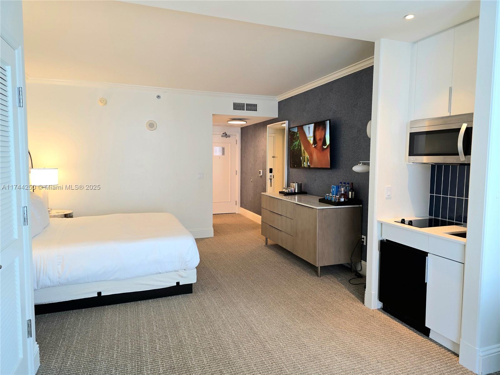 A hotel room features a wall-mounted television, a light wood dresser, and a small kitchenette — 4401 Collins Ave # 1401, Miami Beach FL 33140, MIAMI BEACH, FL