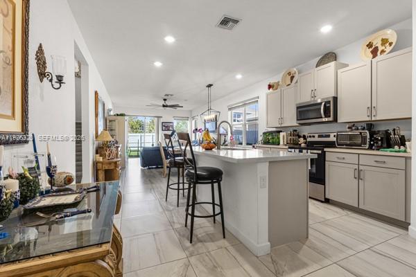 A kitchen with light cabinets and a central island opens into a living area — 13235 SW 270th Ter, Homestead FL 33032, HOMESTEAD, FL