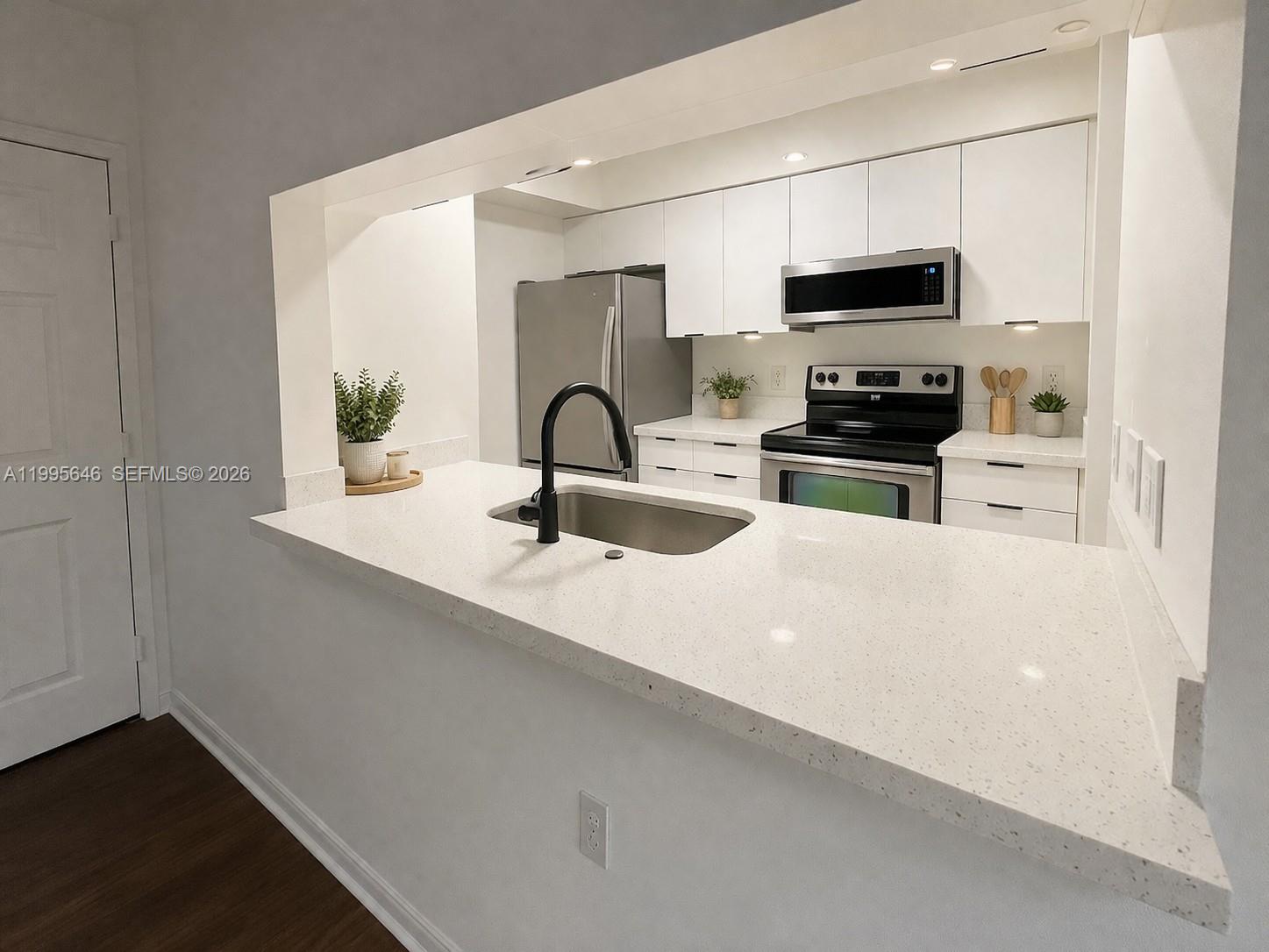 A kitchen features white cabinets, stainless steel appliances, and a white quartz countertop peninsula — 12124 Saint Andrews Pl # 305, Miramar FL 33025, MIRAMAR, FL