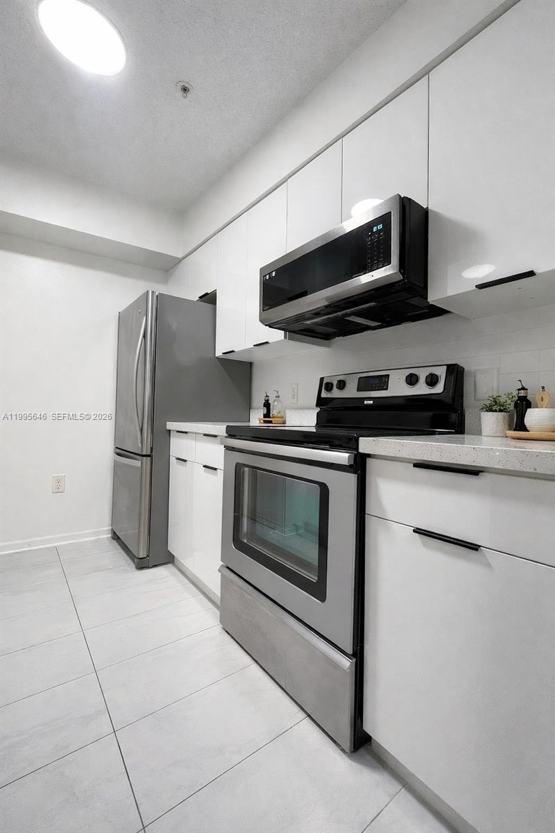 A modern kitchen features white cabinets, stainless steel appliances, and light-colored tile flooring — 12124 Saint Andrews Pl # 305, Miramar FL 33025, MIRAMAR, FL