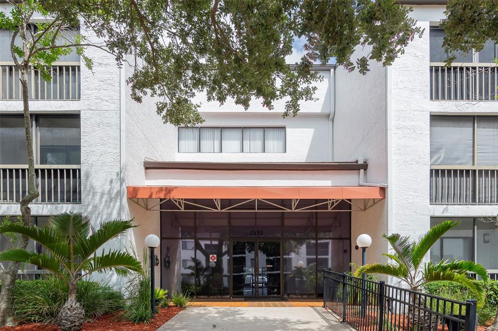 The exterior of a multi-story residential building features a glass entrance under an orange awning — 2595 COUNTRYSIDE BOULEVARD UNIT 8311, CLEARWATER, FL