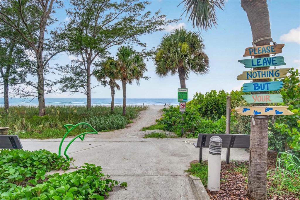 A paved path leads through trees and greenery toward a sandy beach and the ocean — 300 BEACH TRAIL UNIT 201, INDIAN ROCKS BEACH, FL