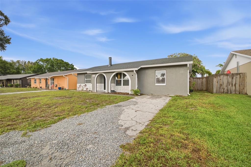 A gray single-story house features a gravel driveway, arched entryway, and a wooden fence — 7941 SMOKETREE COURT, LARGO, FL