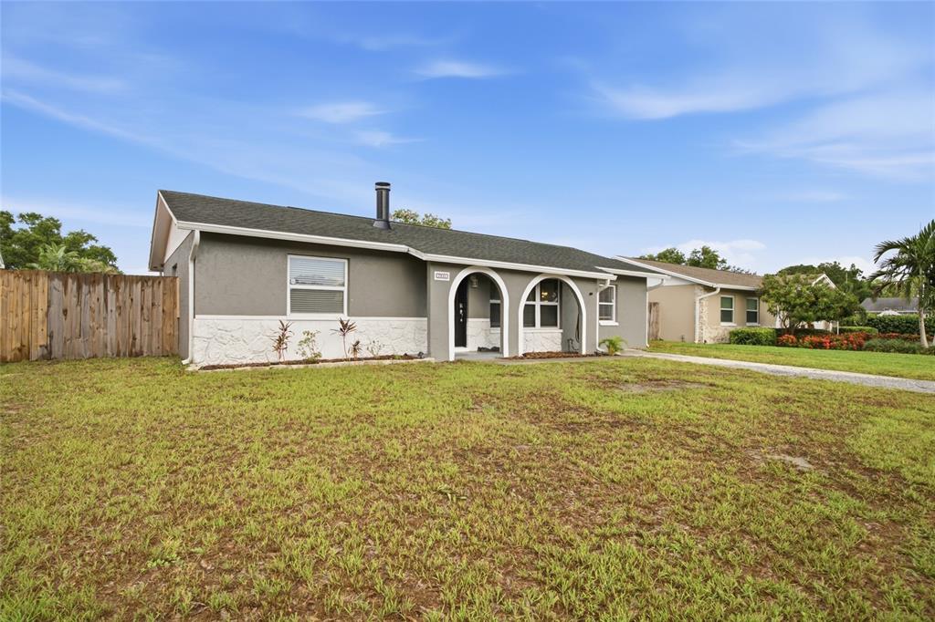 A single-story house with a gray exterior, stone accents, and arched entryways sits on grass — 7941 SMOKETREE COURT, LARGO, FL