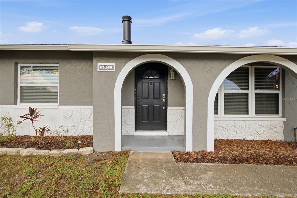 A gray house exterior features a black front door under a white arched entryway — 7941 SMOKETREE COURT, LARGO, FL