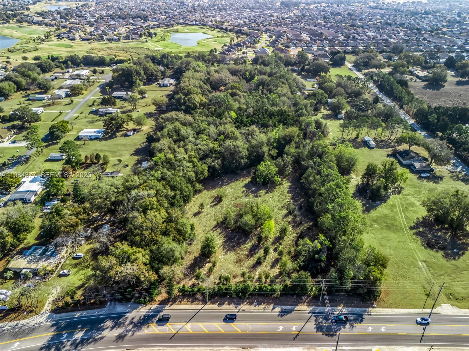 An aerial view shows a vacant, tree-lined lot situated between residential properties and a road — 4942 E County Road 462, Wildwood FL 34785, WILDWOOD, FL