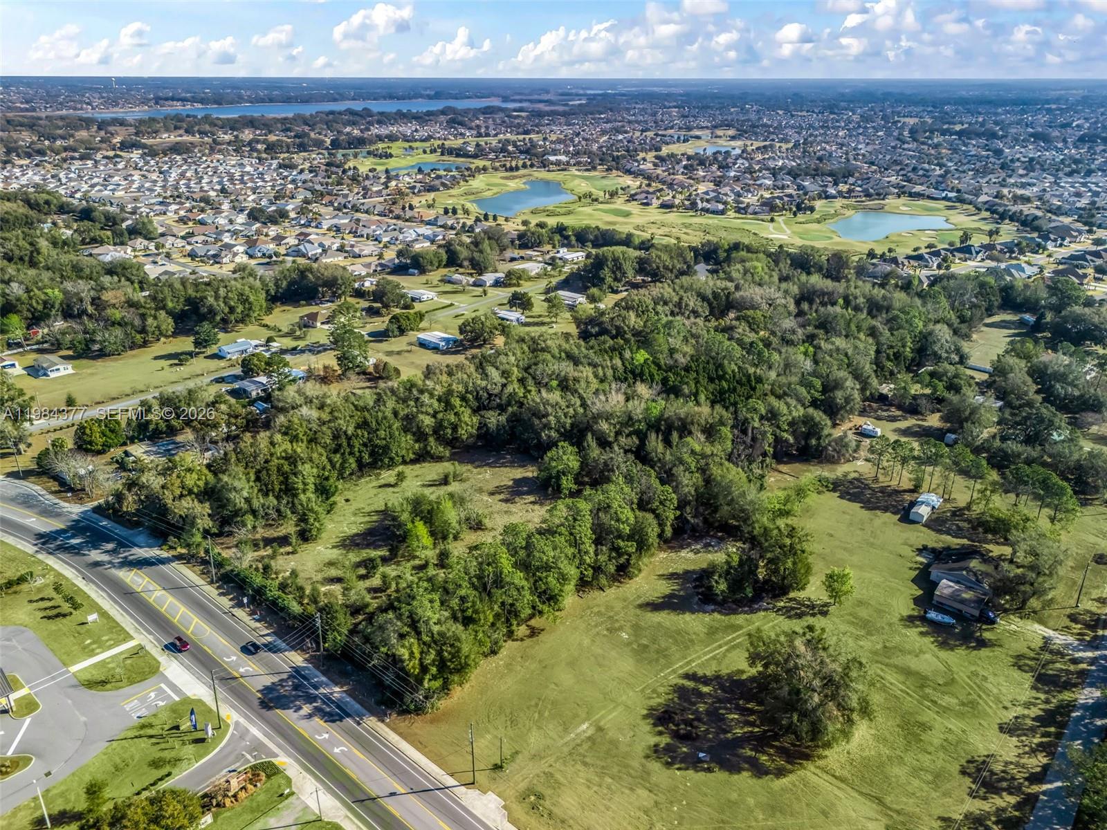 An aerial view shows a large grassy lot bordered by a road and dense trees — 4942 E County Road 462, Wildwood FL 34785, WILDWOOD, FL