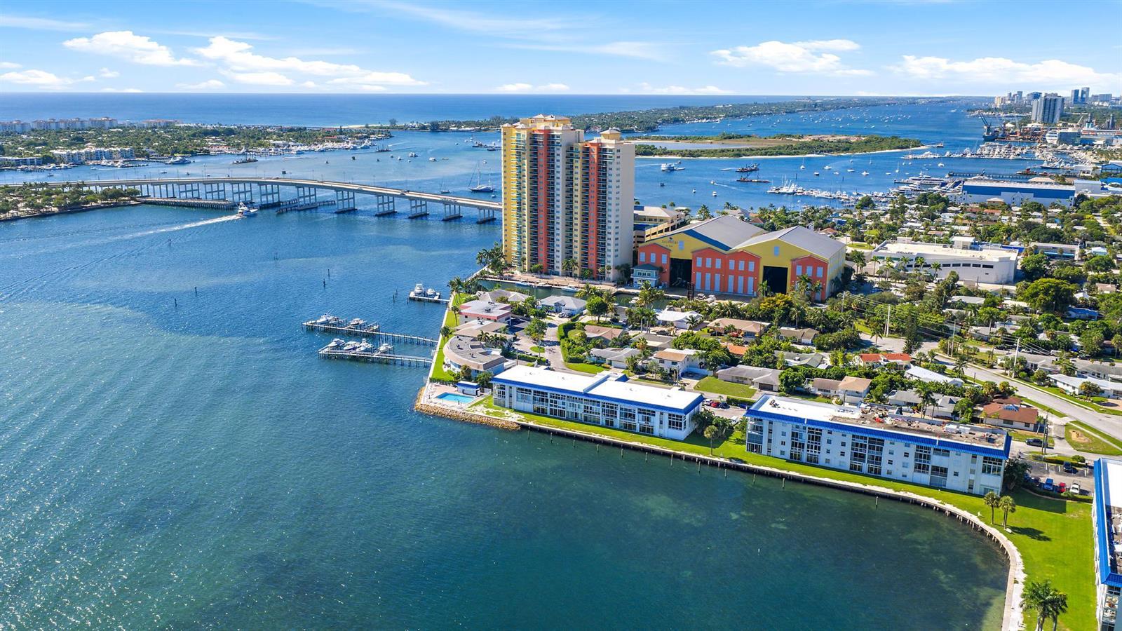 An aerial view shows a waterfront high-rise building, a bridge, and surrounding residential properties — 400 Wilma Circle # 108, Riviera Beach FL 33404, RIVIERA BEACH, FL
