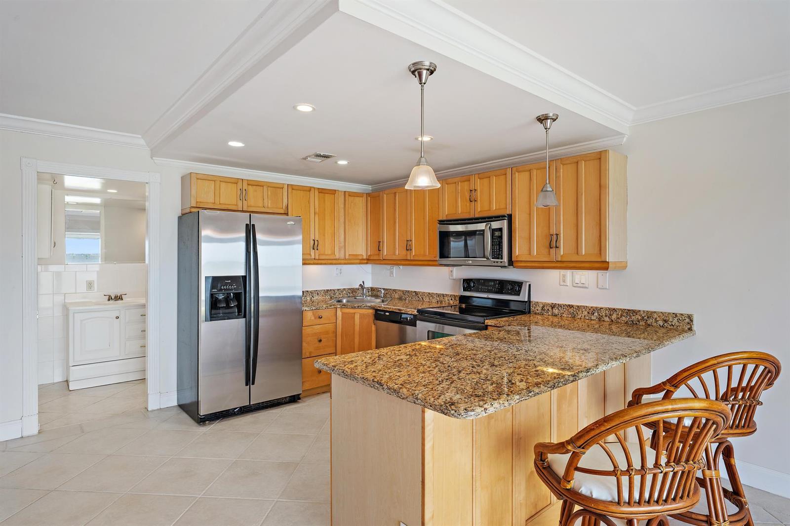 A kitchen features light wood cabinets, granite countertops, stainless steel appliances, and a breakfast bar — 400 Wilma Circle # 108, Riviera Beach FL 33404, RIVIERA BEACH, FL