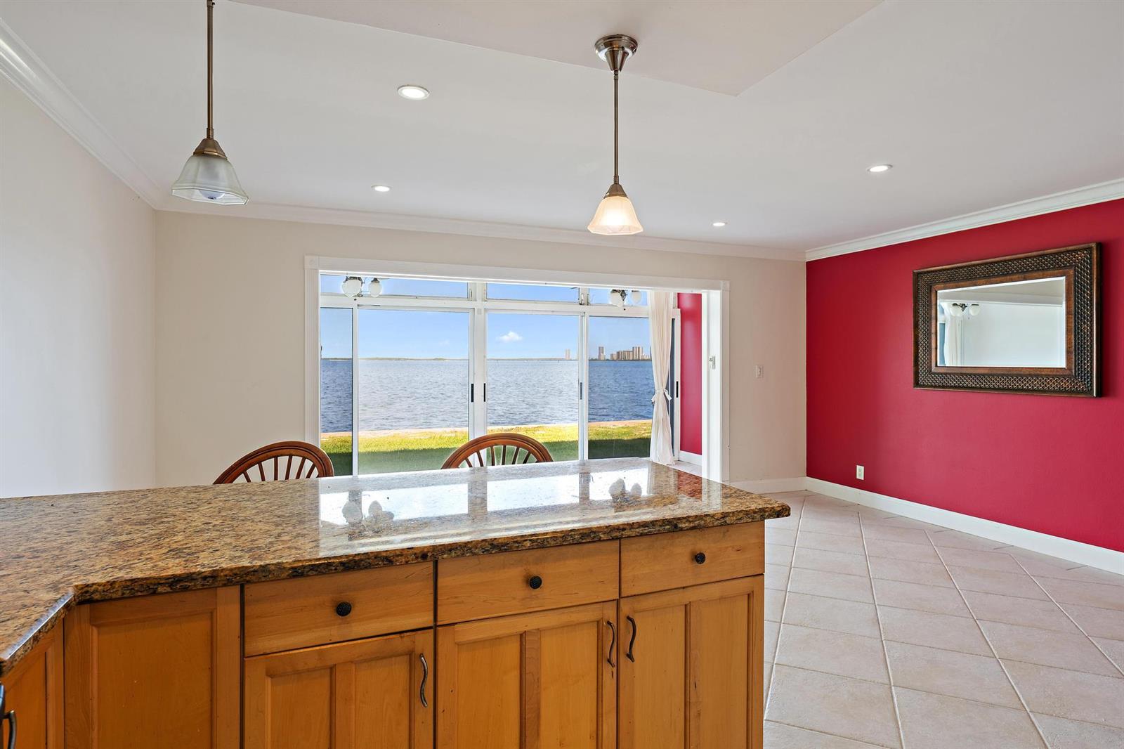 A kitchen island with granite countertops overlooks a room with a red accent wall — 400 Wilma Circle # 108, Riviera Beach FL 33404, RIVIERA BEACH, FL