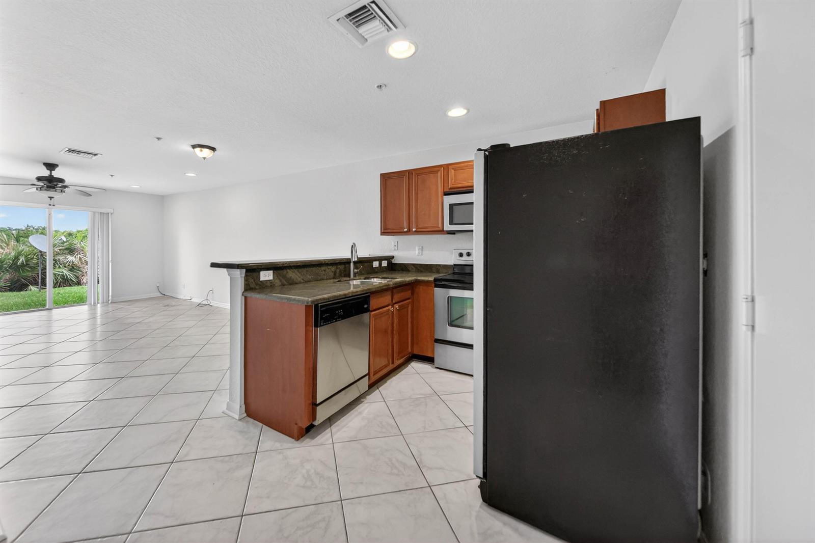 A kitchen with wood cabinets, granite countertops, and stainless steel appliances opens to a living area — 5313 SE Jennings Lane, Stuart FL 34997, STUART, FL