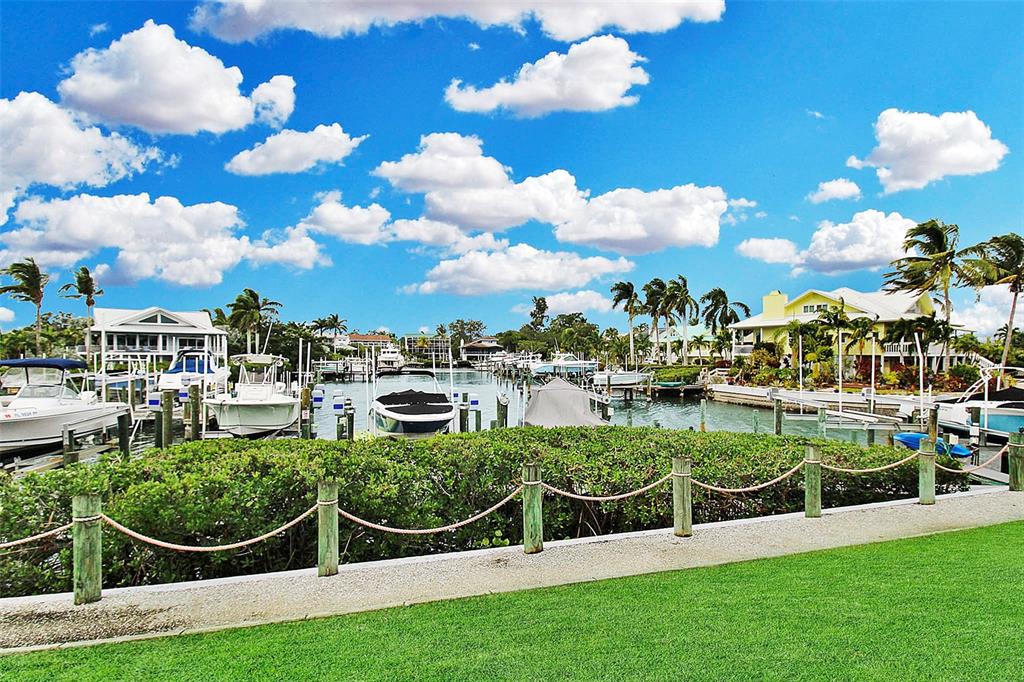A waterfront view of a boat dock with several docked boats and tropical landscaping — 1343 SIESTA BAYSIDE DRIVE UNIT 1343-C, SARASOTA, FL