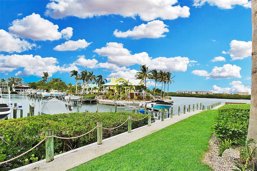 A waterfront view shows a yellow house, boat docks, and a grassy lawn with fencing — 1343 SIESTA BAYSIDE DRIVE UNIT 1343-C, SARASOTA, FL