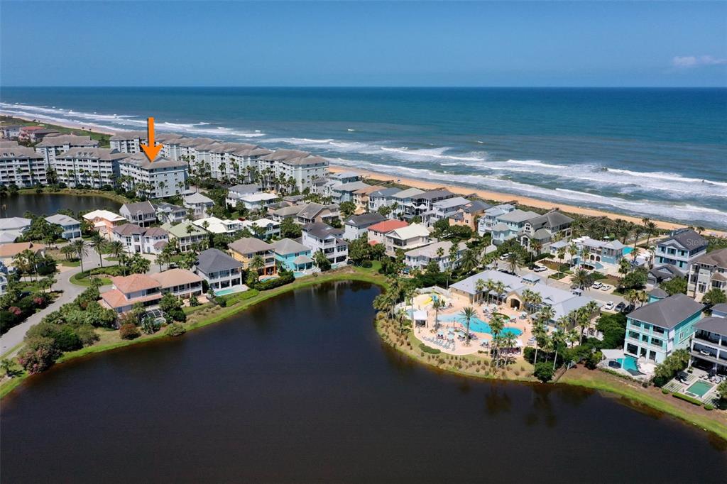 An aerial view shows a coastal community with a large pool, lake, and oceanfront condos — 1000 CINNAMON BEACH WAY UNIT 941, PALM COAST, FL