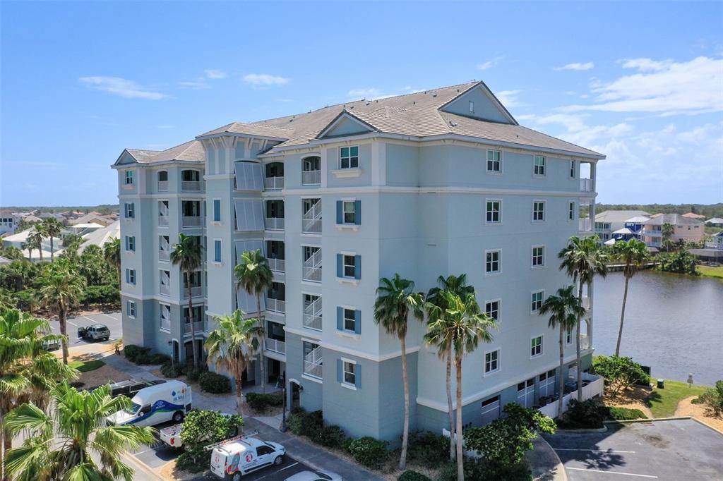 An aerial view of a multi-story, light blue residential building with palm trees and parking — 1000 CINNAMON BEACH WAY UNIT 941, PALM COAST, FL